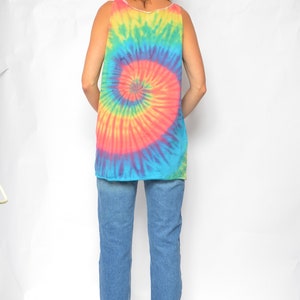 Puede incluir: Una mujer con un top sin mangas de tie-dye con un patr&oacute;n de espiral azul, rosa, amarillo y verde. Tambi&eacute;n lleva pantalones vaqueros azules y zapatos de tac&oacute;n negros.