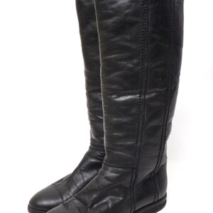 May include: A pair of black leather knee-high boots with a pointed toe and a low heel.