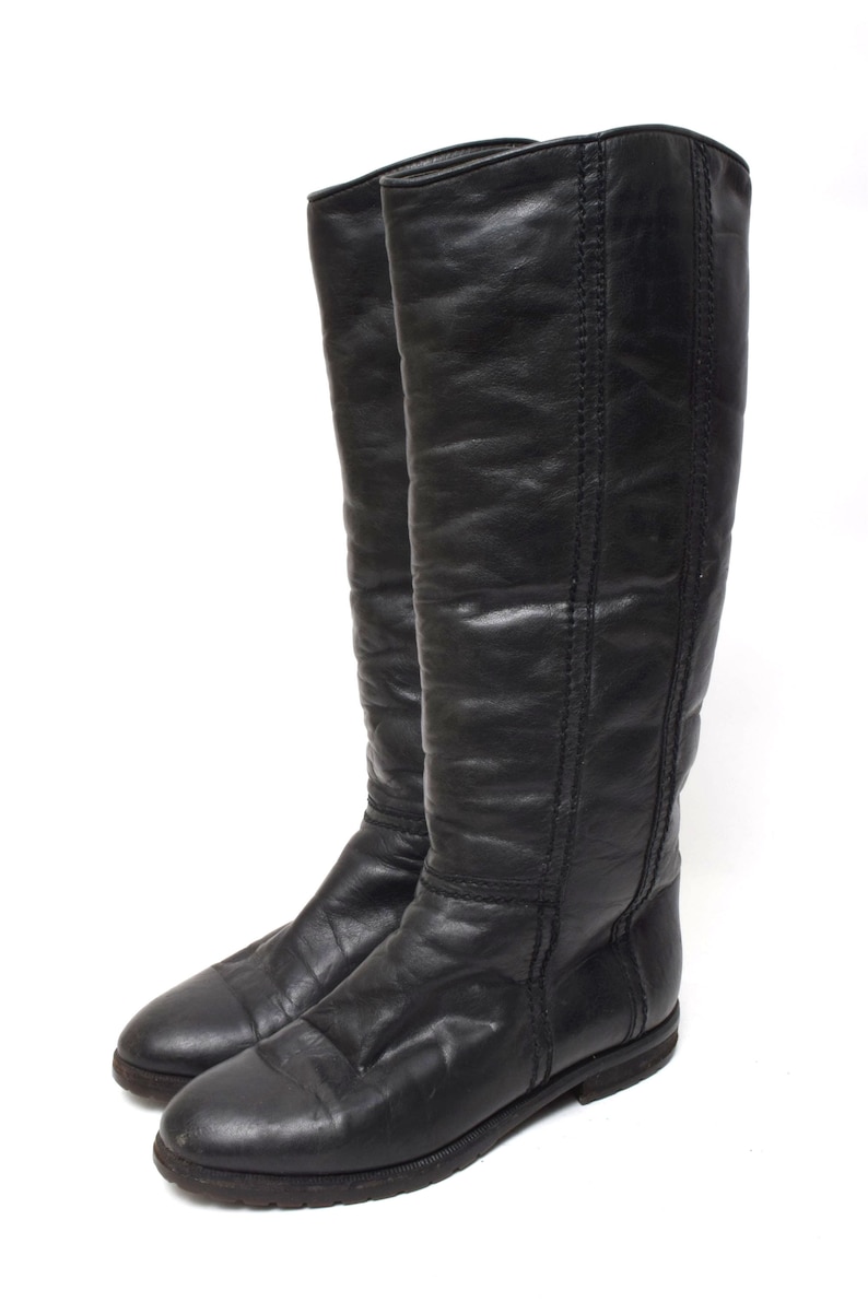 May include: A pair of black leather knee-high boots with a pointed toe and a low heel.