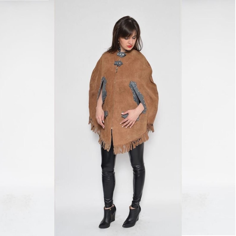 May include: A brown suede cape with fringe detailing and a zipper closure. The cape has leather accents with silver studs.