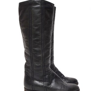 May include: A pair of black leather knee-high boots with a pointed toe and a low heel.