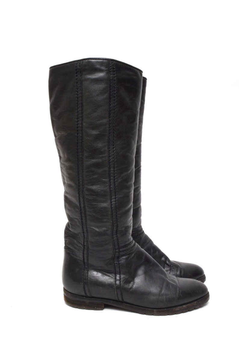 May include: A pair of black leather knee-high boots with a pointed toe and a low heel.