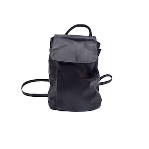 Puede incluir: Una mochila de cuero negro con cierre de solapa, un asa superior y correas ajustables para los hombros. El bolso tiene una base estructurada y un acabado liso y mate, ofreciendo un diseño limpio y funcional para llevar objetos personales.