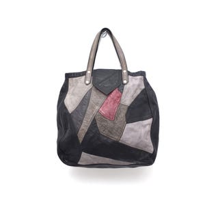Könnte beinhalten: Eine Patchwork-Tragetasche aus Leder mit geometrischem Design. Die Tasche kombiniert schwarze, graue und rosa Lederflicken. Sie hat zwei graue Griffe und silberne Nieten. Die Tasche ist zum Tragen von Gegenständen konzipiert.
