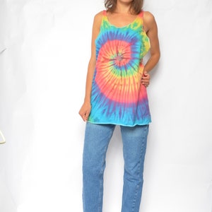 Puede incluir: Una mujer con un top sin mangas de tie-dye con un patr&oacute;n de espiral arco&iacute;ris y jeans azules. Lleva zapatos de tac&oacute;n azules.