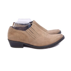 Peut inclure: Une paire de bottines en daim marron clair à bout pointu et talon bas. Les bottines présentent un motif de surpiqûres décoratif sur la pointe et un design à enfiler.