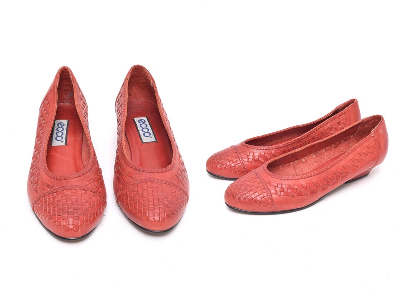 May include: A pair of red woven leather ballet flats. The shoes have a rounded toe and a low heel. The brand name "ecco" is visible on the insole. The shoes are displayed on a white background.