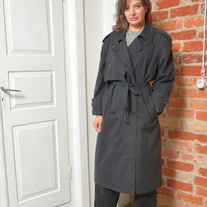 May include: A black trench coat with a belted waist and button closure. The coat features a classic design with a collar, shoulder epaulettes, and pockets. The coat is knee-length and appears to be made of a lightweight material.