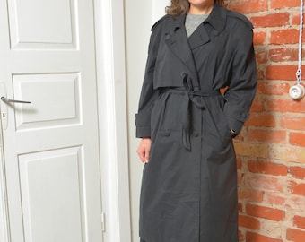 May include: A black trench coat with a belted waist and button closure. The coat features a classic design with a collar, shoulder epaulettes, and pockets. The coat is knee-length and appears to be made of a lightweight material.