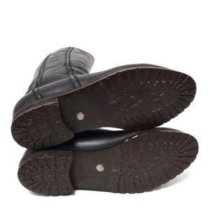 May include: A pair of black leather boots with a brown rubber sole. The boots have a zipper on the back and a stitched seam on the front.