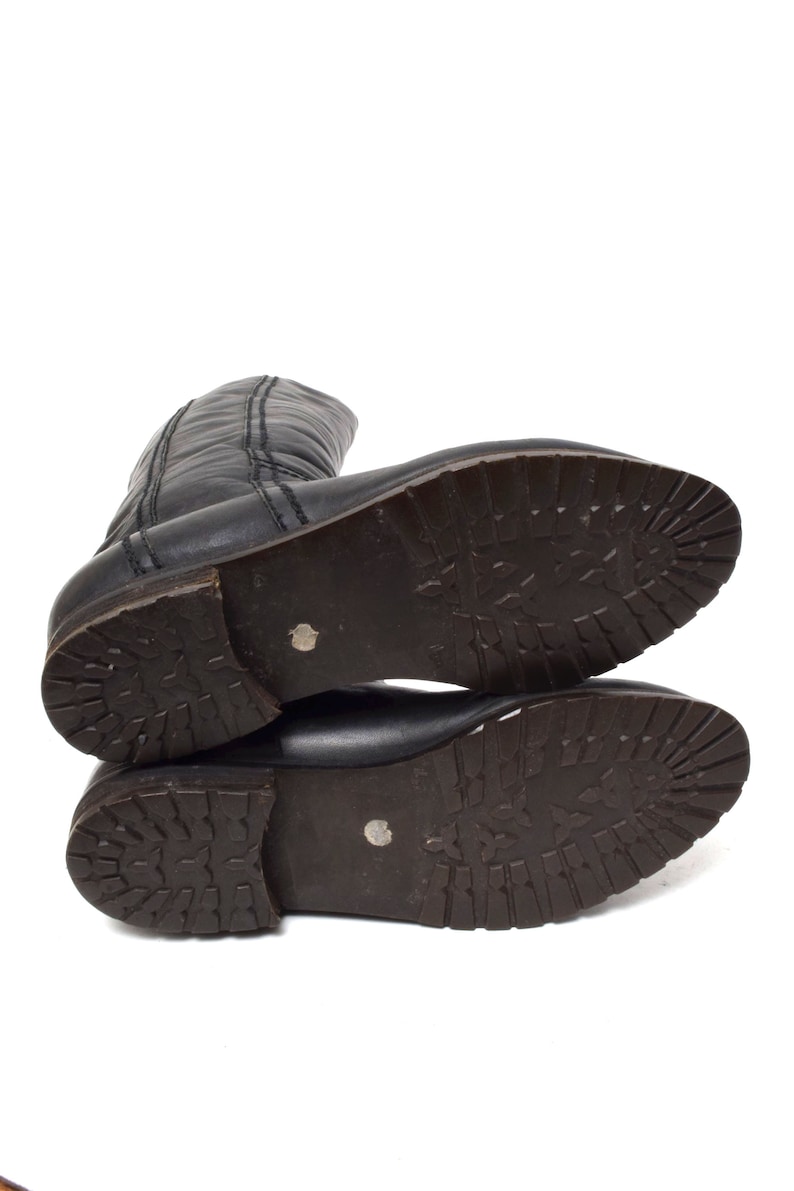 May include: A pair of black leather boots with a brown rubber sole. The boots have a zipper on the back and a stitched seam on the front.
