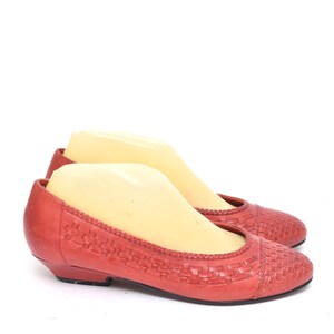May include: A pair of coral-colored flats with a woven design on the toe and vamp. The shoes have a low heel and a rounded toe. The shoes are displayed on a white background.