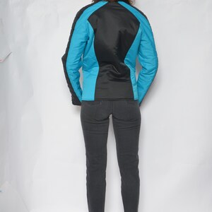 May include: A black and turquoise jacket with a zipper closure. The jacket has a quilted design and is worn over a pair of dark denim jeans.