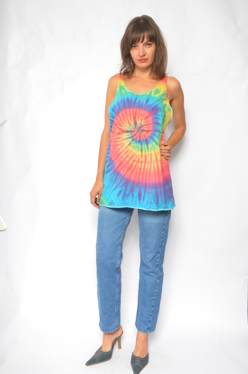 Puede incluir: Una mujer con un top sin mangas de tie-dye con un patr&oacute;n de espiral arco&iacute;ris y pantalones vaqueros azules. Lleva zapatos de tac&oacute;n azul oscuro.