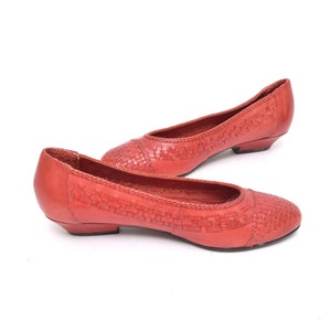 May include: A pair of coral-colored flats with a woven design on the toe and vamp. The shoes have a low heel and a rounded toe. The shoes are made of leather.