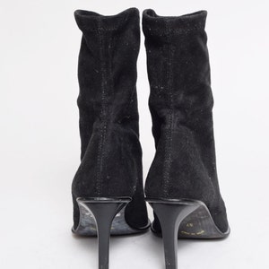 May include: A pair of black suede heeled boots with a pointed toe. The boots have a stretchy upper and a high heel.
