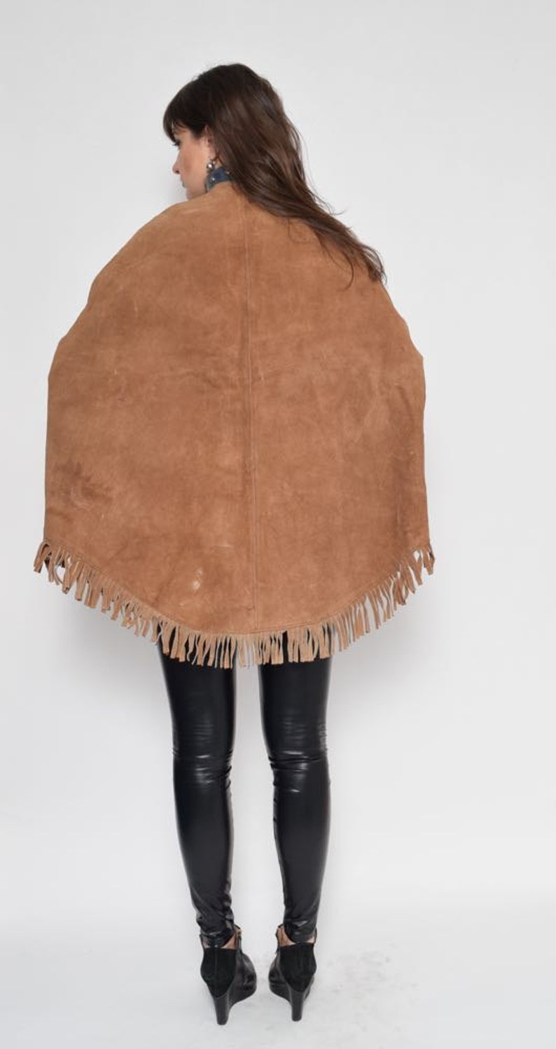 May include: A brown suede cape with fringe trim. The cape is worn over black leggings and black heeled boots.