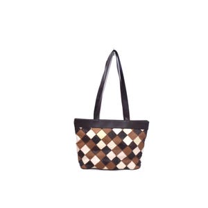 May include: A tote bag with a geometric pattern. The bag features a patchwork design of brown, black, and cream-colored diamond shapes. It has a dark brown leather top and matching handles. The bag is set against a white background.