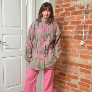 Puede incluir: Chaqueta multicolor con estampados rosas, verdes y azules. La chaqueta tiene cuello alto, bolsillos y cintura ajustable. La persona lleva pantalones rosas.