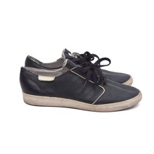 May include: A pair of black leather low-top trainers with white laces. The shoes have a white rubber sole and a black leather upper.