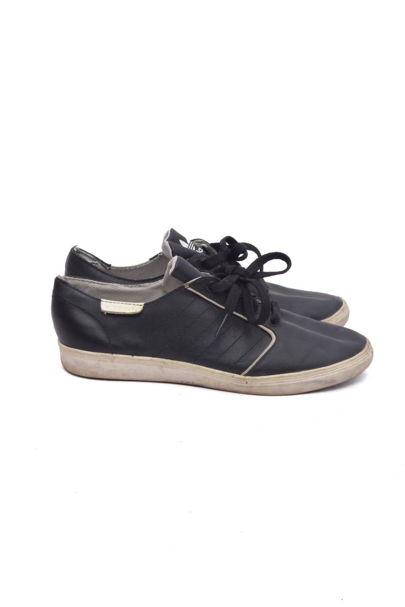 May include: A pair of black leather low-top trainers with white laces. The shoes have a white rubber sole and a black leather upper.