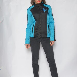 May include: A black and blue jacket with a zipper closure and a logo that says "HBS" on the front. The jacket has a stand-up collar and long sleeves. The person wearing the jacket is also wearing black jeans and blue shoes.