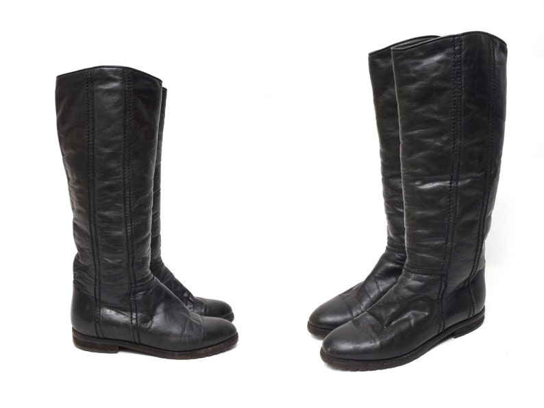 May include: A pair of black leather knee-high boots with a pointed toe and a low heel.