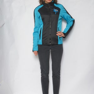 May include: A woman wearing a black and blue jacket with a zipper closure and a logo on the chest. She is wearing black pants and blue shoes.