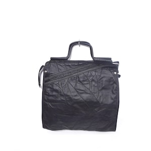 May include: A black leather satchel bag with a unique textured design and a top handle.