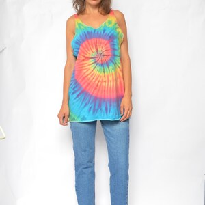 Puede incluir: Un top sin mangas de tie-dye con un patr&oacute;n de espiral arco&iacute;ris. El top es sin mangas y tiene un escote redondo. La modelo lleva pantalones vaqueros azules y tacones azul oscuro.