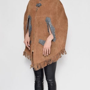 May include: A brown suede cape with fringe detailing and silver accents. The cape has a zipper closure and a stand-up collar.