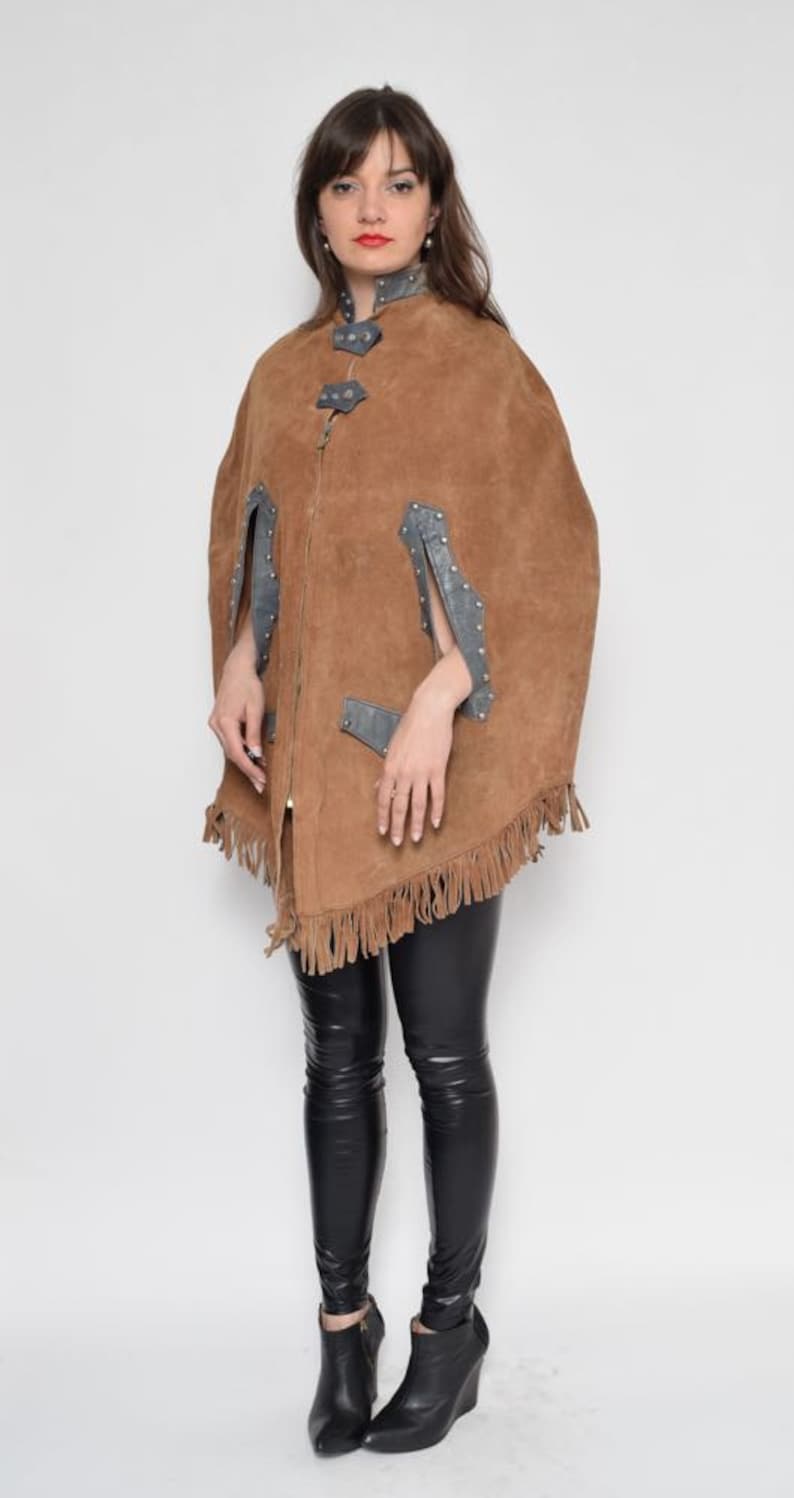 May include: A brown suede cape with fringe detailing and silver accents. The cape has a zipper closure and a stand-up collar.