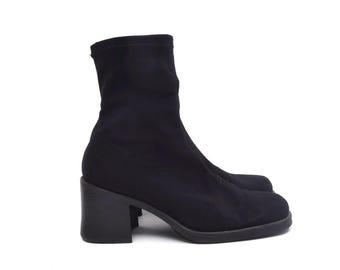 May include: Black ankle boots with a block heel. The boots are made of a stretchy fabric and have a pointed toe.