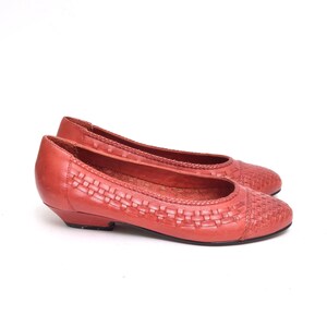 May include: A pair of red leather flats with a woven design on the vamp. The shoes have a low heel and a rounded toe. The flats are set against a white background.