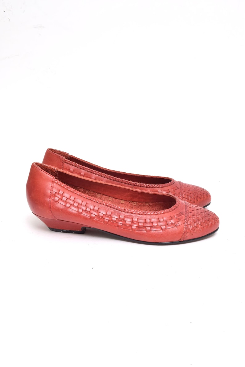 May include: A pair of red leather flats with a woven design on the vamp. The shoes have a low heel and a rounded toe. The flats are set against a white background.