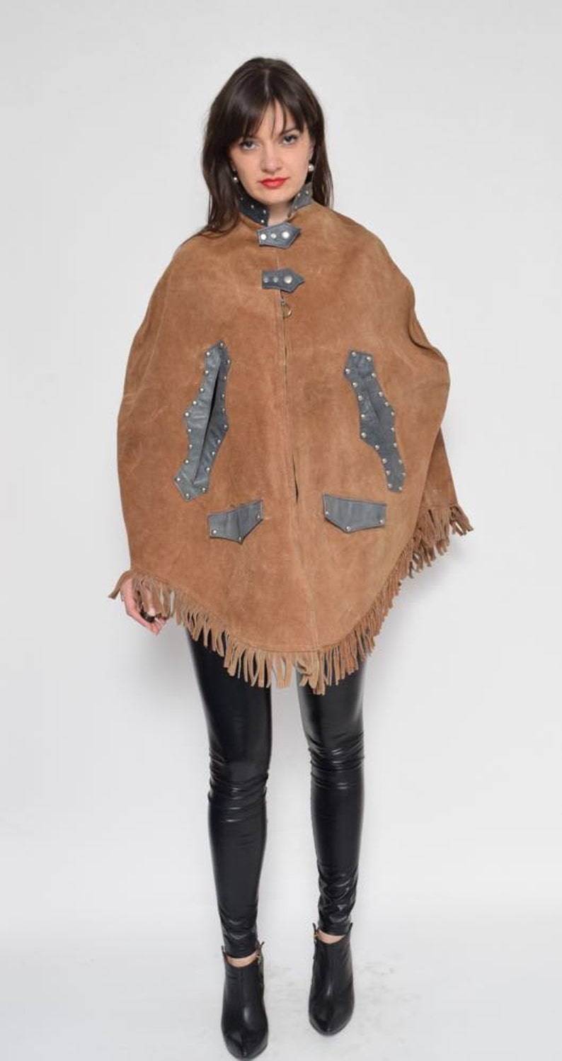 May include: A brown suede poncho with fringe and black leather accents. The poncho has a zipper closure and a stand-up collar.