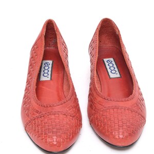 May include: A pair of red leather ballet flats with a woven pattern on the toe and sides. The shoes have a pointed toe and a low heel. The brand name "ecco" is visible on the insole.