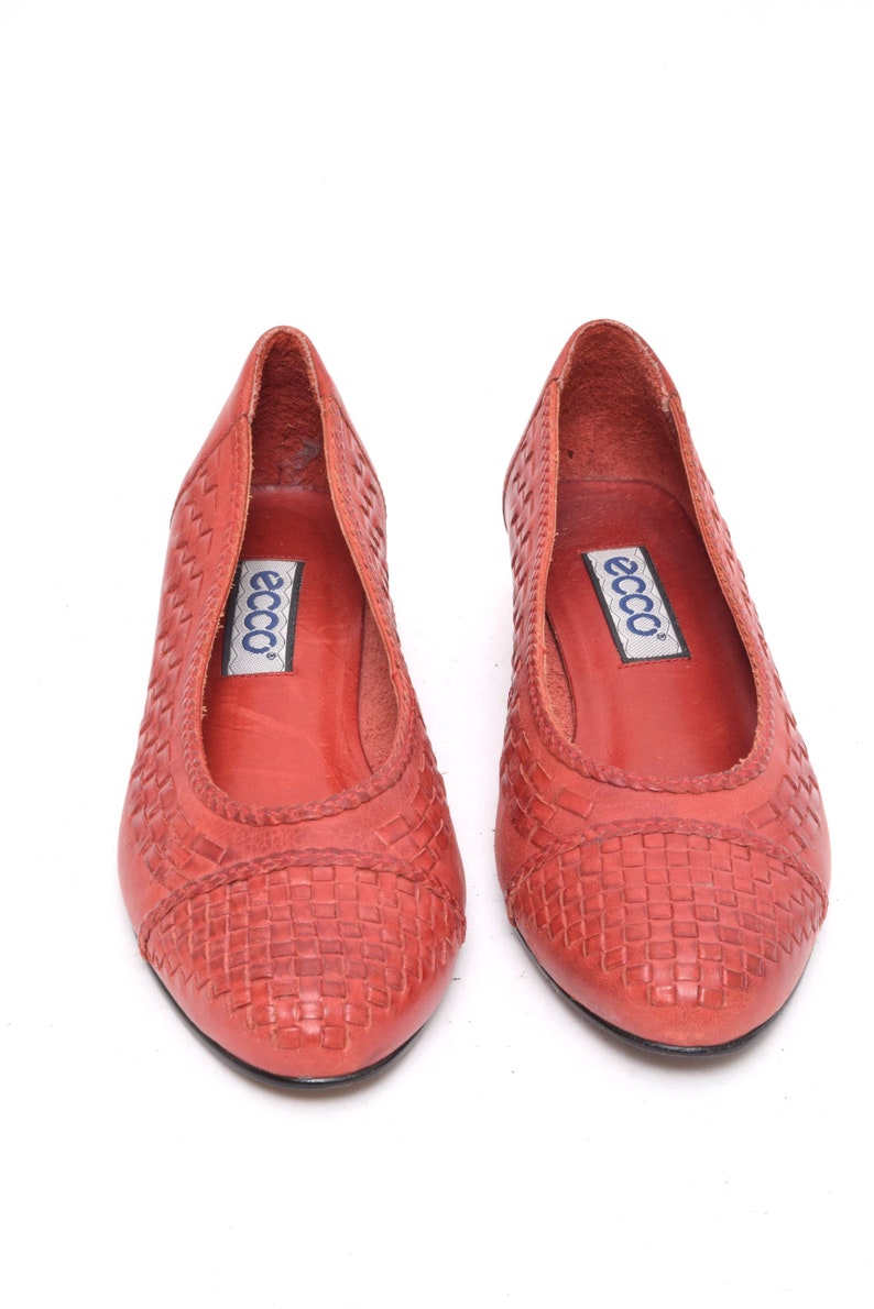 May include: A pair of red leather ballet flats with a woven pattern on the toe and sides. The shoes have a pointed toe and a low heel. The brand name "ecco" is visible on the insole.