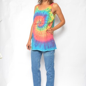Puede incluir: Una mujer con un top sin mangas de tie-dye con un dise&ntilde;o de espiral azul, rosa, amarillo y naranja. Tambi&eacute;n lleva pantalones vaqueros azules y zapatos de tac&oacute;n azul oscuro.
