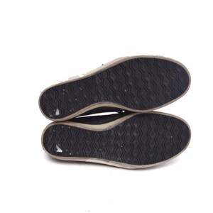 May include: The underside of a pair of black canvas shoes with a white rubber sole. The sole has a textured pattern.