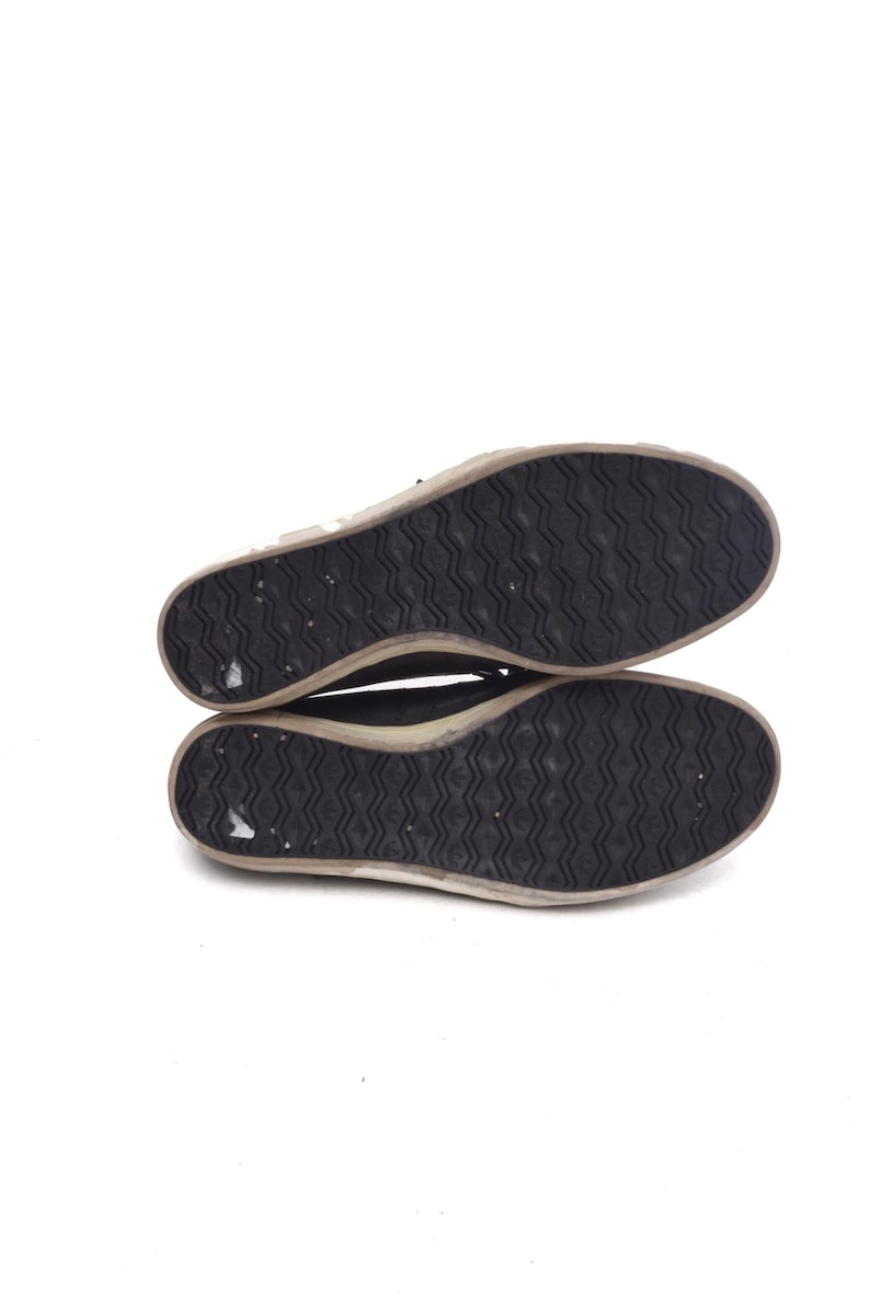 May include: The underside of a pair of black canvas shoes with a white rubber sole. The sole has a textured pattern.