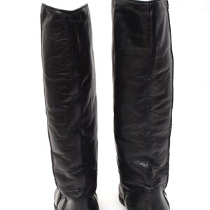 May include: A pair of black leather knee-high boots with a pointed toe and a low heel.