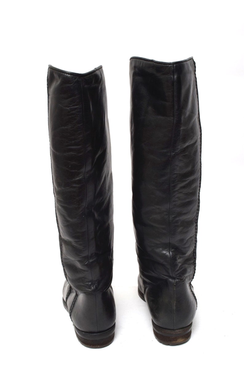 May include: A pair of black leather knee-high boots with a pointed toe and a low heel.