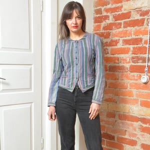 Könnte beinhalten: Vintage Jacke mit vertikalen Streifen in Blau, Grün und Rot. Die Jacke hat einen runden Kragen, einen Knopfverschluss und zwei kleine Vordertaschen. Das Model trägt eine schwarze Jeans.