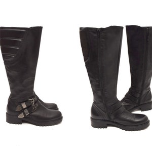 May include: A pair of black leather knee-high boots with silver buckles. The boots have a zip on the inside of each boot.