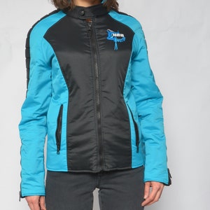 May include: A black and turquoise blue jacket with a zipper closure. The jacket has a logo on the left side that says "X-MAS Motors".