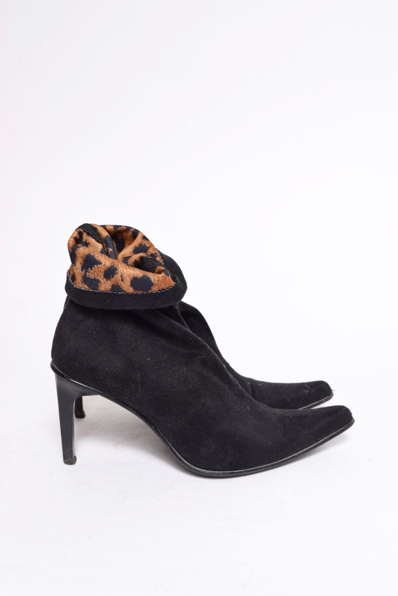 May include: Black suede heeled boots with a leopard print cuff. The boots have a pointed toe and a stiletto heel.