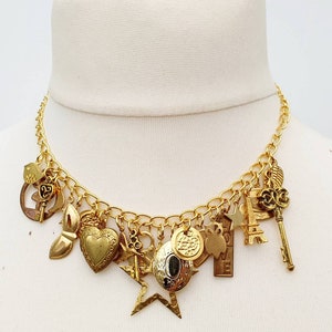 May include: A gold chain necklace with multiple charms, including a heart, a star, a key, and a bird. The charms are all gold-toned and have intricate details.