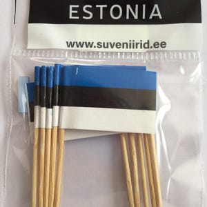 May include: A package of toothpick flags featuring the Estonian flag design. The flags are blue, black, and white, with the word "ESTONIA" printed on the packaging. The website address www.suveniriid.ee is also visible.