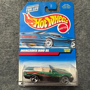 May include: A Hot Wheels Mercedes 500 SL die-cast toy car on a blue and white card. The car is green with red and gold accents. The card features the Hot Wheels logo and the text "GUARANTEED FOR LIFE".